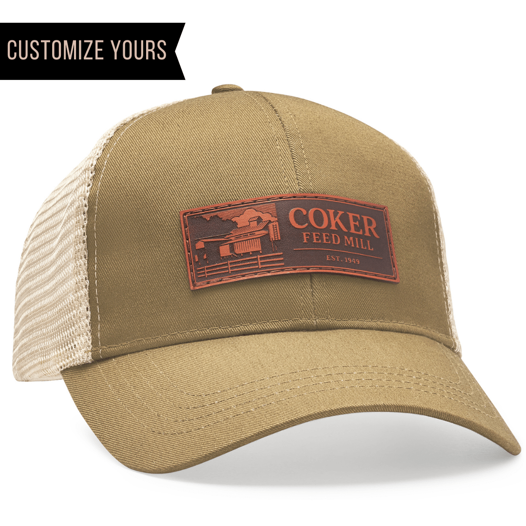 The Econscious EC7070 is a tan trucker hat made of organic cotton and recycled polyester, featuring a brown patch with Coker Feed Mill Est. 1949 and a barn illustration. Customize yours with your company logo for the perfect branded accessory.