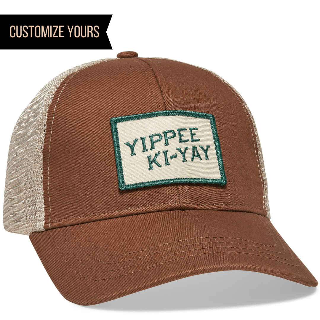 A sustainable organic cotton and recycled polyester trucker hat by Econscious, featuring a green-bordered YIPPEE KI-YAY patch in brown and beige. Customize it with your company logo using the Customize Yours feature for bulk orders.