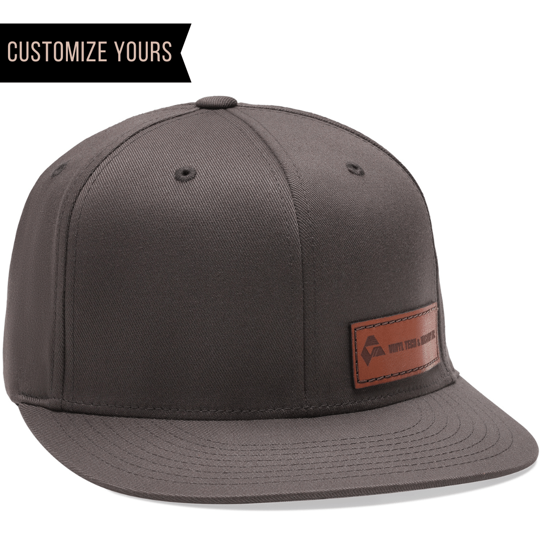 The Flexfit 6297F, a gray snapback with a brown leather patch for logos, features small embossed text. A black banner at the top left says CUSTOMIZE YOURS in white, offering personalization. Perfect for corporate branding with bulk custom orders.