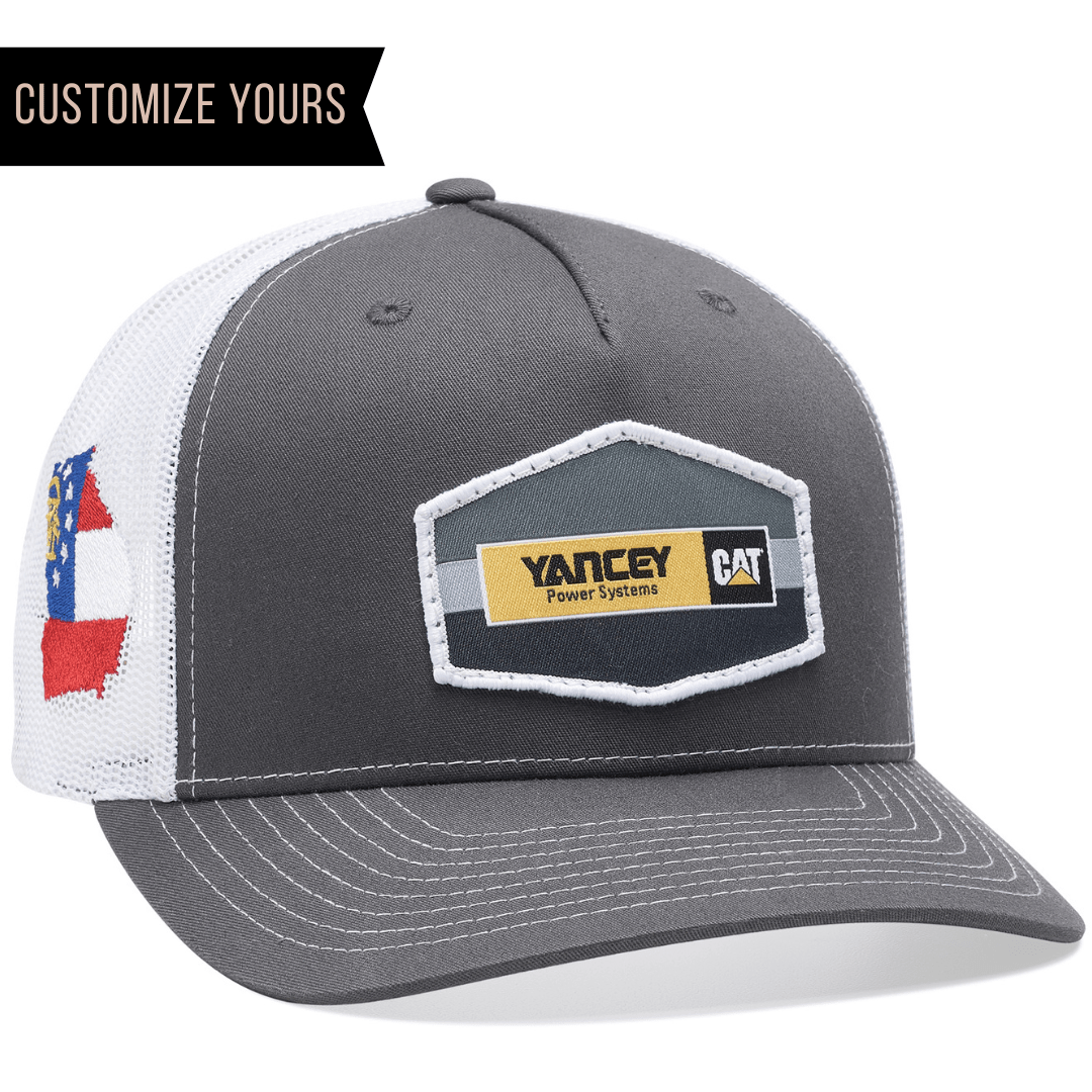 The Richardson 112FP is a gray and white 5-panel snapback trucker hat featuring a mesh back with a Yancey Power Systems CAT patch on the front, a flag patch on the side, and Customize Yours in the top left corner, making it ideal for branded hats.