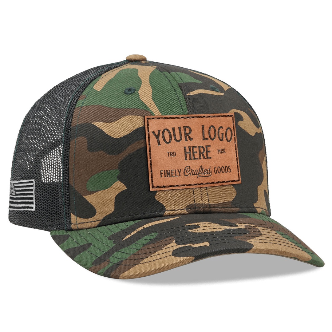 The Richardson 112P Printed Trucker Hat by Richardson is a camouflage cap with a black mesh back, featuring white embroidered text Custom Your Logo Here and an American flag patch on the brims side, perfect for branded or company logo hats.