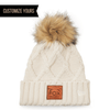 customizable logo on ivory New Era 911 faux fur pom  with cable knit beanie with genuine sustainable veg tan leather patch custom logo in bulk online