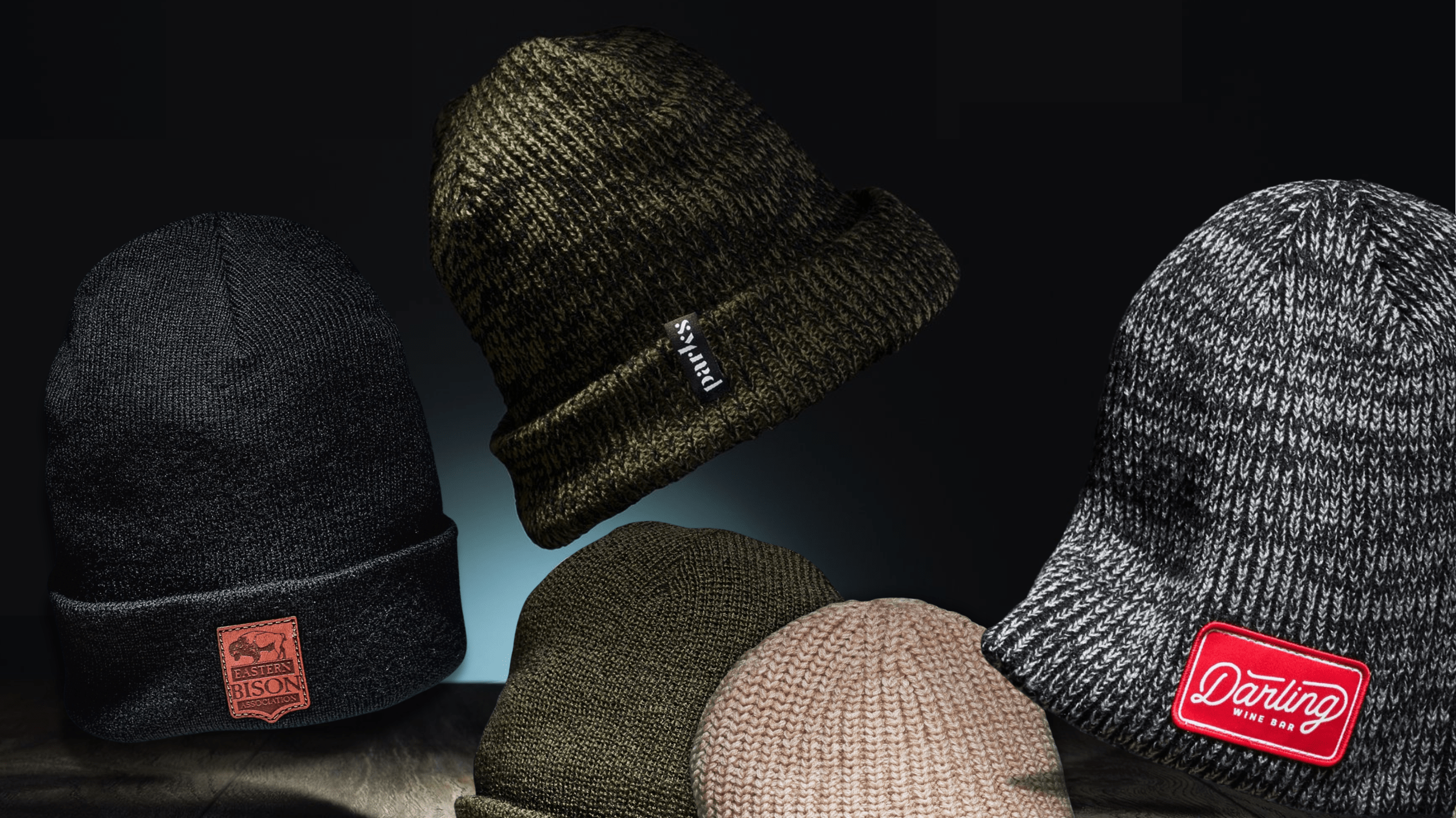 quality custom beanies with logo for business in bulk green beanie with woven tag, marled beanie with red embroidered patch and black cuffed beanie with leather patch made to order in usa